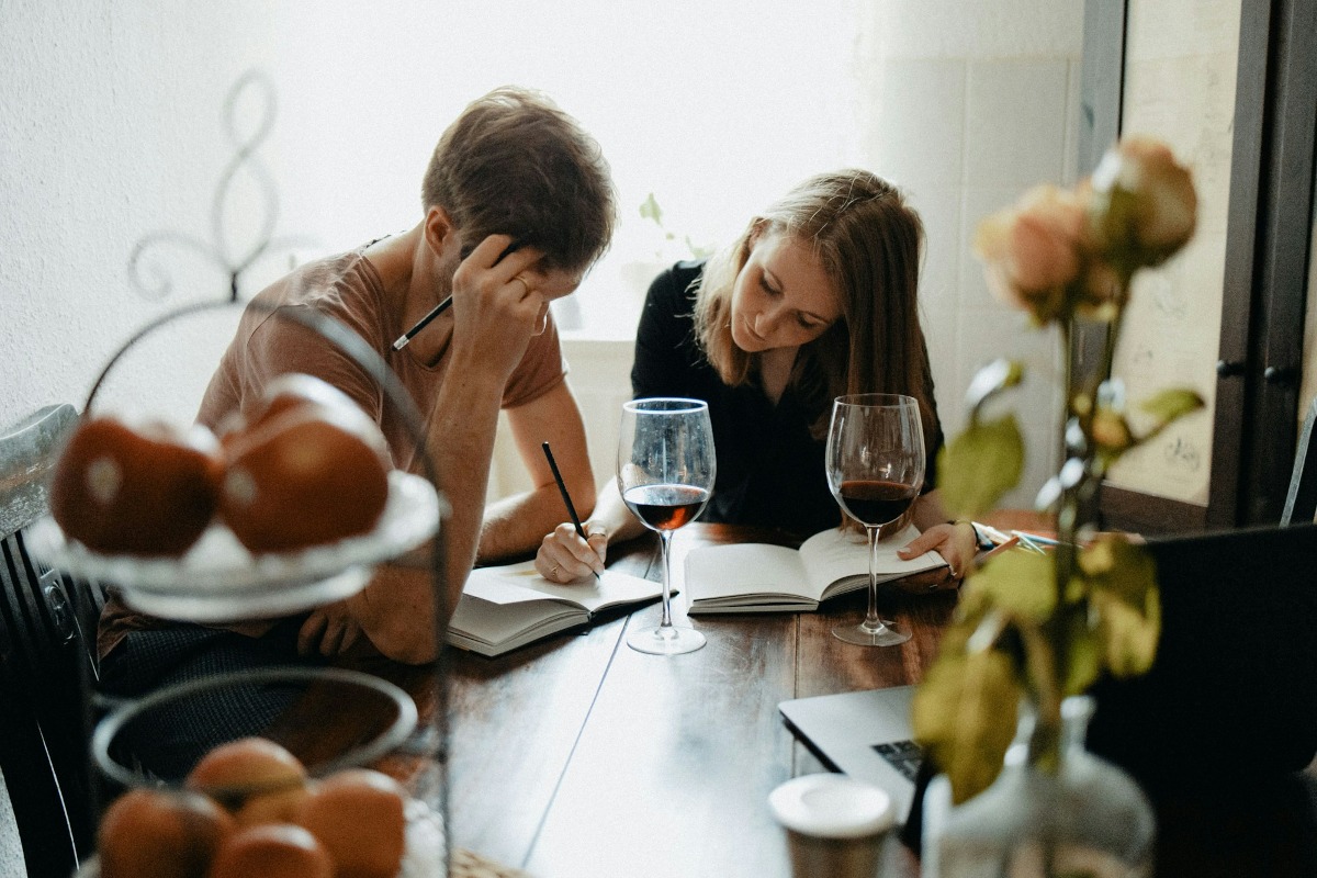 Een man en vrouw zitten aan tafel en bestuderen samen documenten, met glazen water en fruit op tafel.