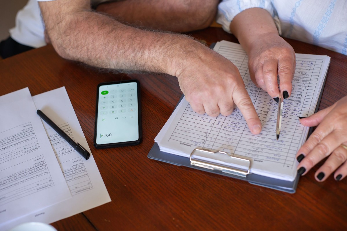 Handen werken aan financiële planning met documenten en smartphone calculator op houten tafel.