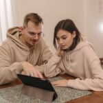 Jong stel bestudeert financiële informatie op een tablet thuis.