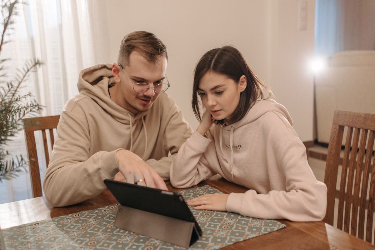 Jong stel bestudeert financiële informatie op een tablet thuis.